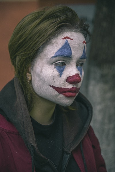 A sad woman whose face is painted as a clown. Photo by Den Trushtin