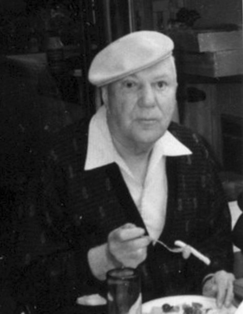 an older Bill Olssen, holding a fork, wearing a beret
