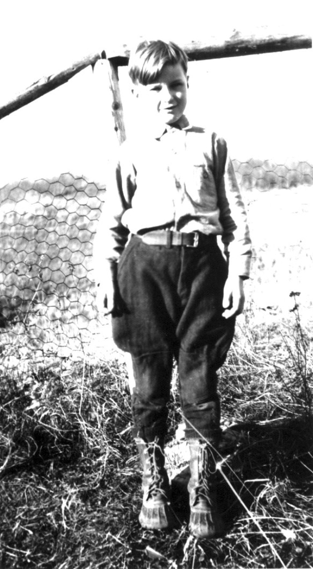 Boy in boots and Jodhpurs trousers standing before a chicken-wire fence
