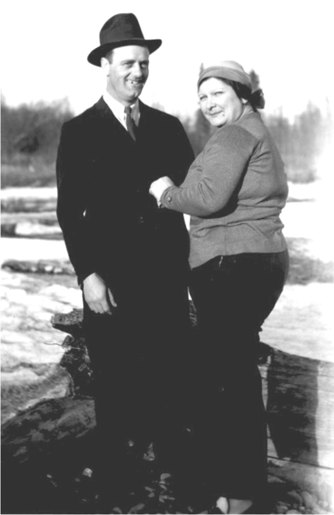 Smiling man in suit and hat, woman facing him turning her head toward the camera