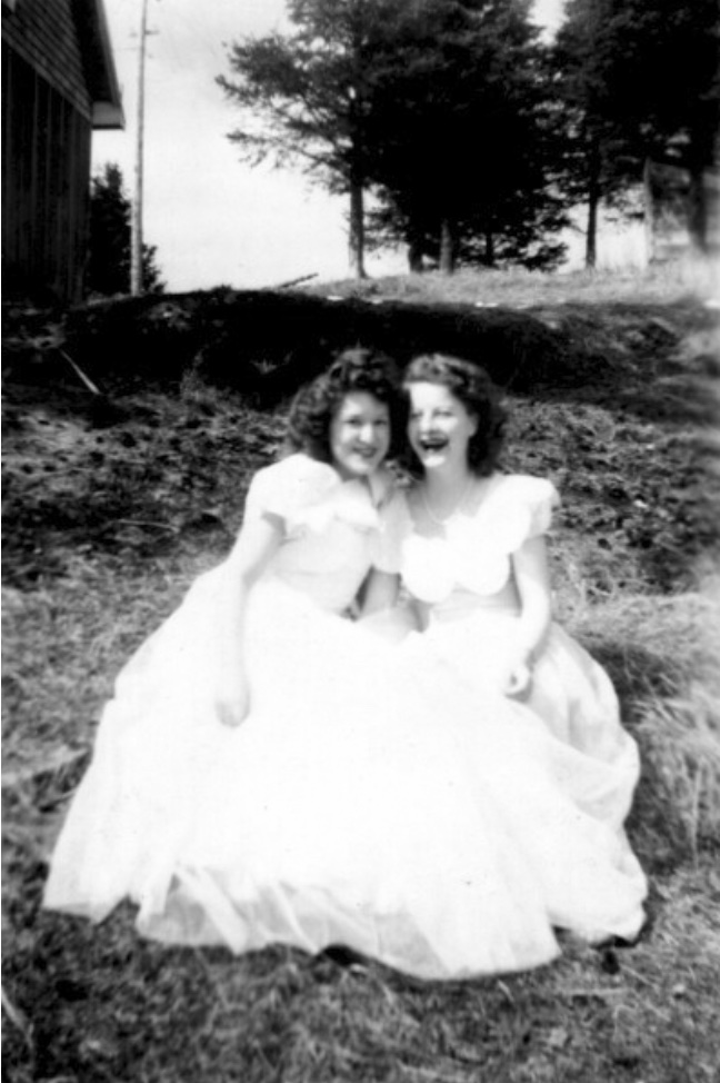 Two young women in big white dresses seated on a grassy hillside