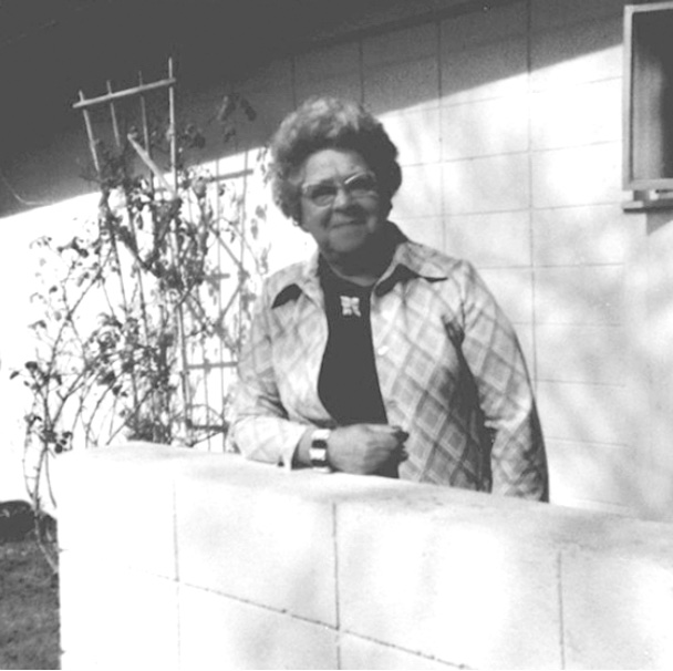 Woman leaning on a cinderblock wall, wearing glasses and a light jacket