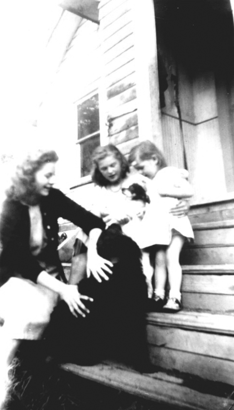 Two young women with a girl and two dogs on wooden steps