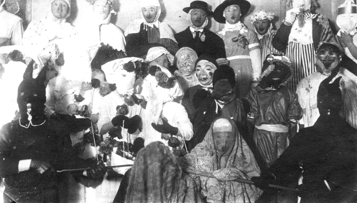 Over a dozen people in costumes and masks; two in rabbit masks in the front holding poles as if to restrain the crowd