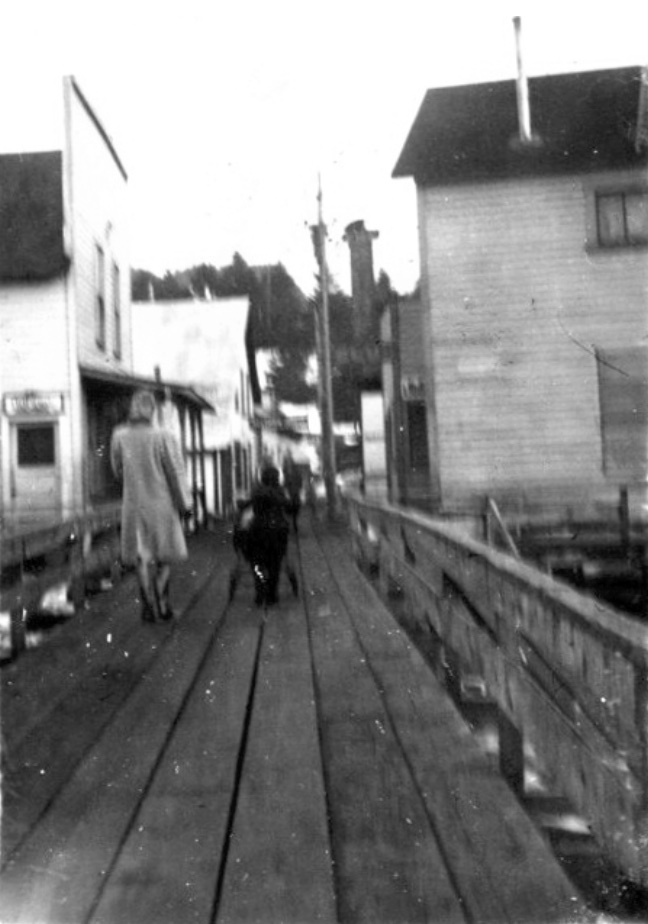 Boardwalk, a woman in overcoat and a child with a cart, a store on the left