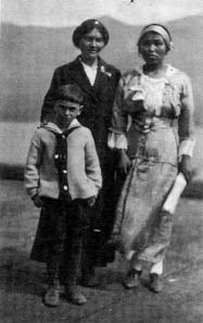 Two women and a boy, the woman on the left has her right hand on the shoulder of the boy, both women are in dresses