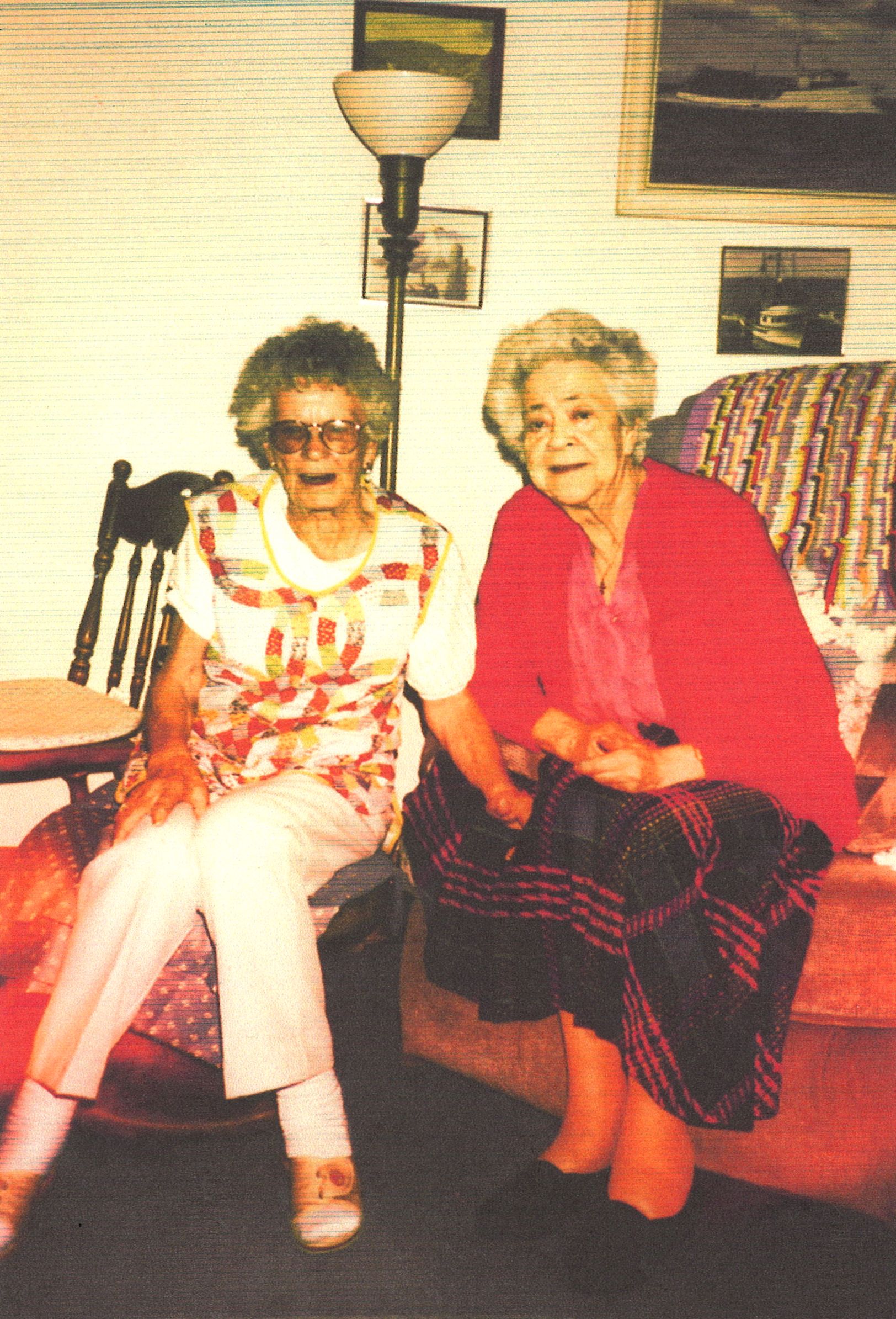Two old aunts, seated, in a living room; photos of boats on the wall.