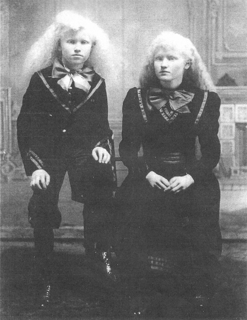Two young people with long white hair and large bow ties, sitting